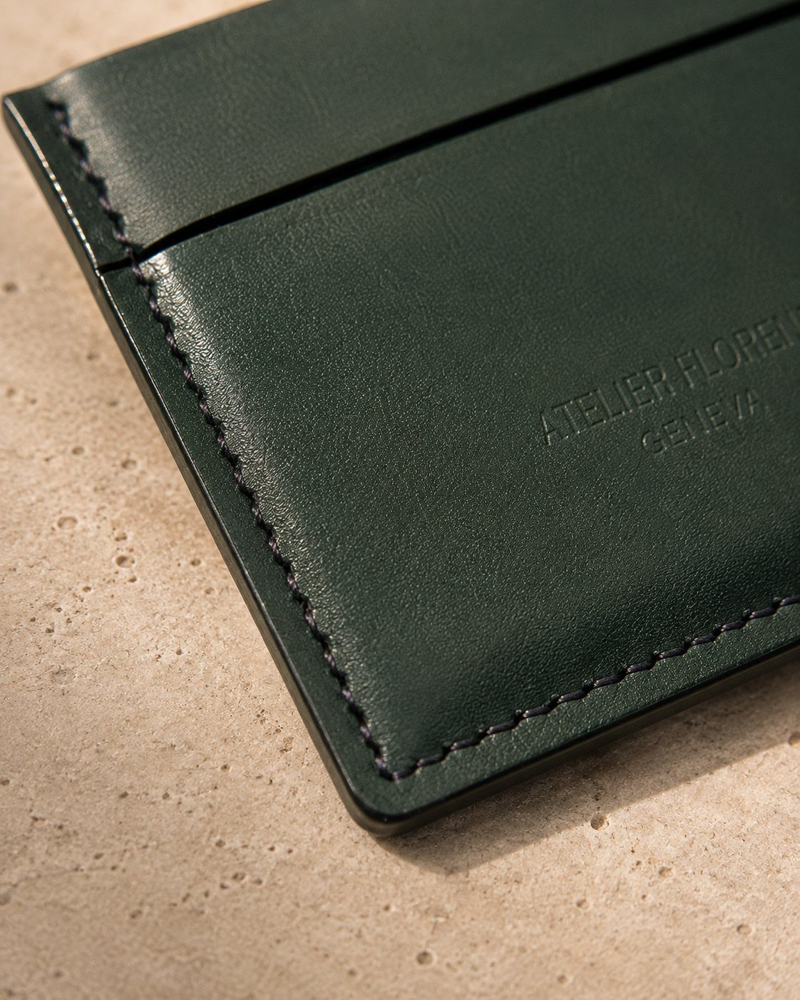 Détail de la texture et des coutures du porte-cartes rive compact en cuir vert foncé