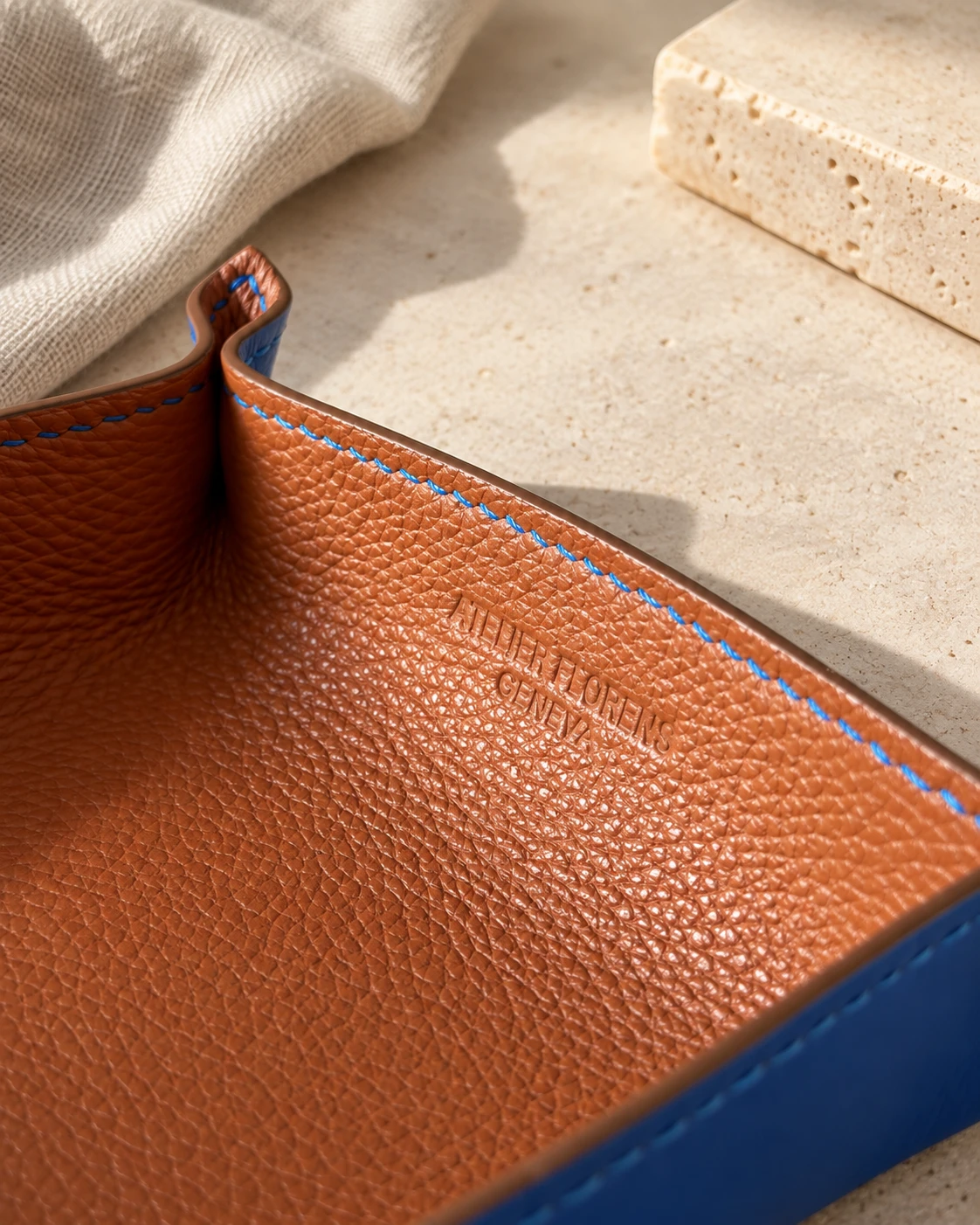 Détail d'un vide-poche en cuir cognac à couture bleue, marqué Atelier Florens